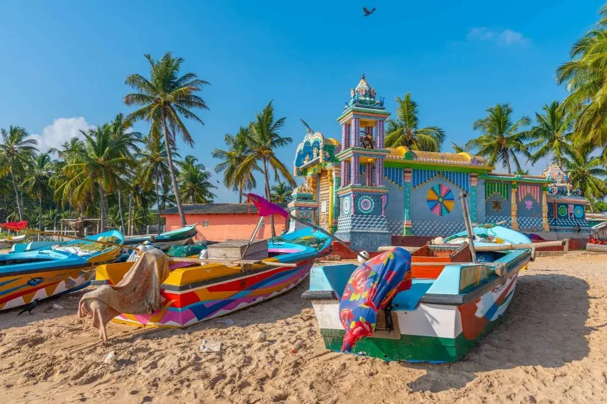 Barcas coloridas en la playa de Sri Lanka, con un templo vibrante al fondo. Es seguro viajar a Sri Lanka y disfrutar de su belleza.