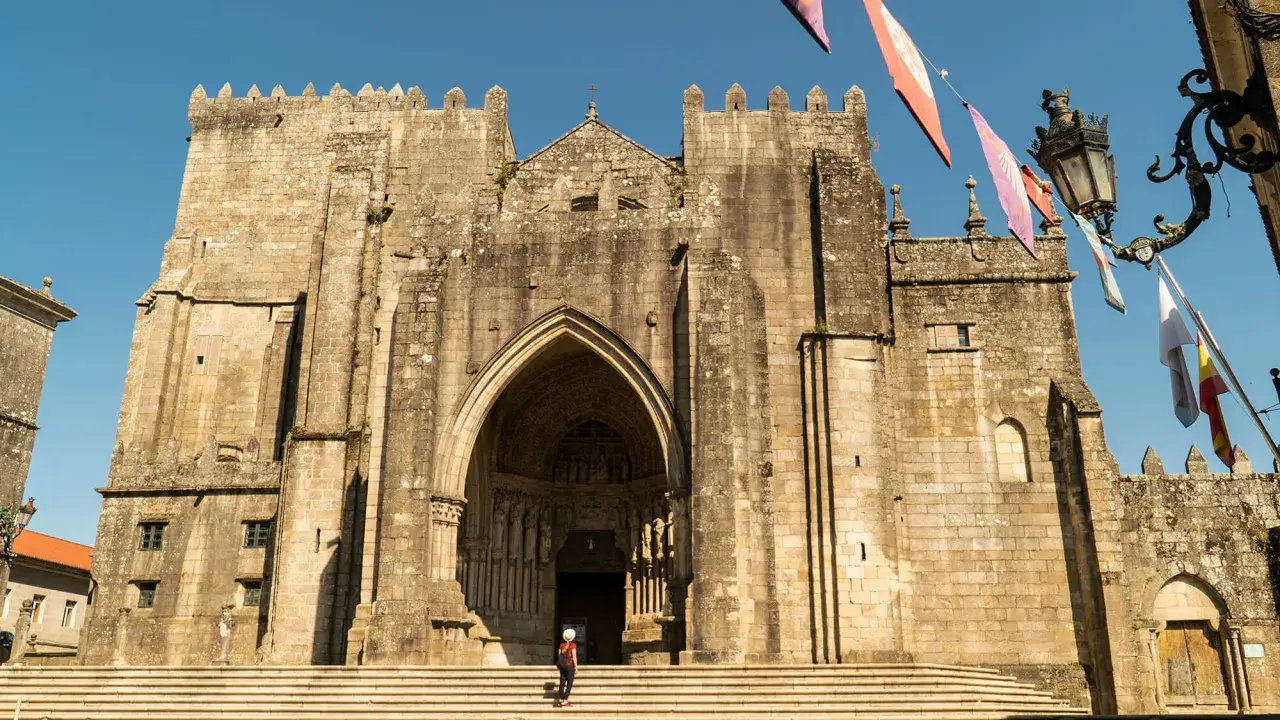 Impresionante Catedral de Tui, un lugar imprescindible que ver en Tui. Fachada de piedra con arco gótico y una persona en las escaleras.