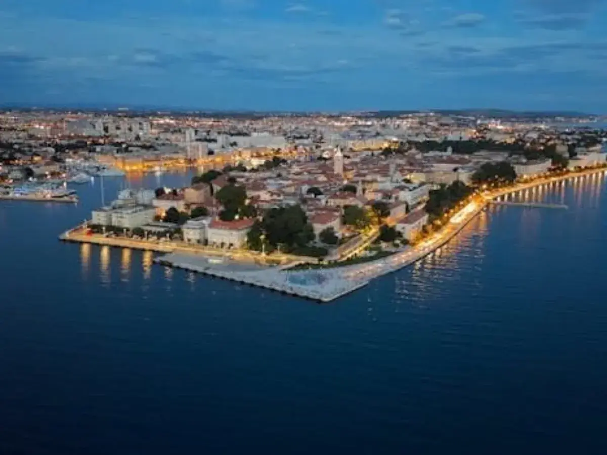 Vista aérea de Zadar al anochecer. La ciudad iluminada se extiende a lo largo de la costa, con el mar Adriático en primer plano. ¡Mucho que ver en Zadar!