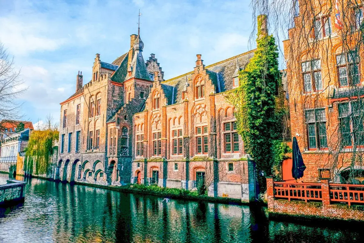 Edificios históricos de ladrillo a lo largo de un canal, reflejando la belleza de Brujas, un viaje inolvidable de Bruselas a Brujas.