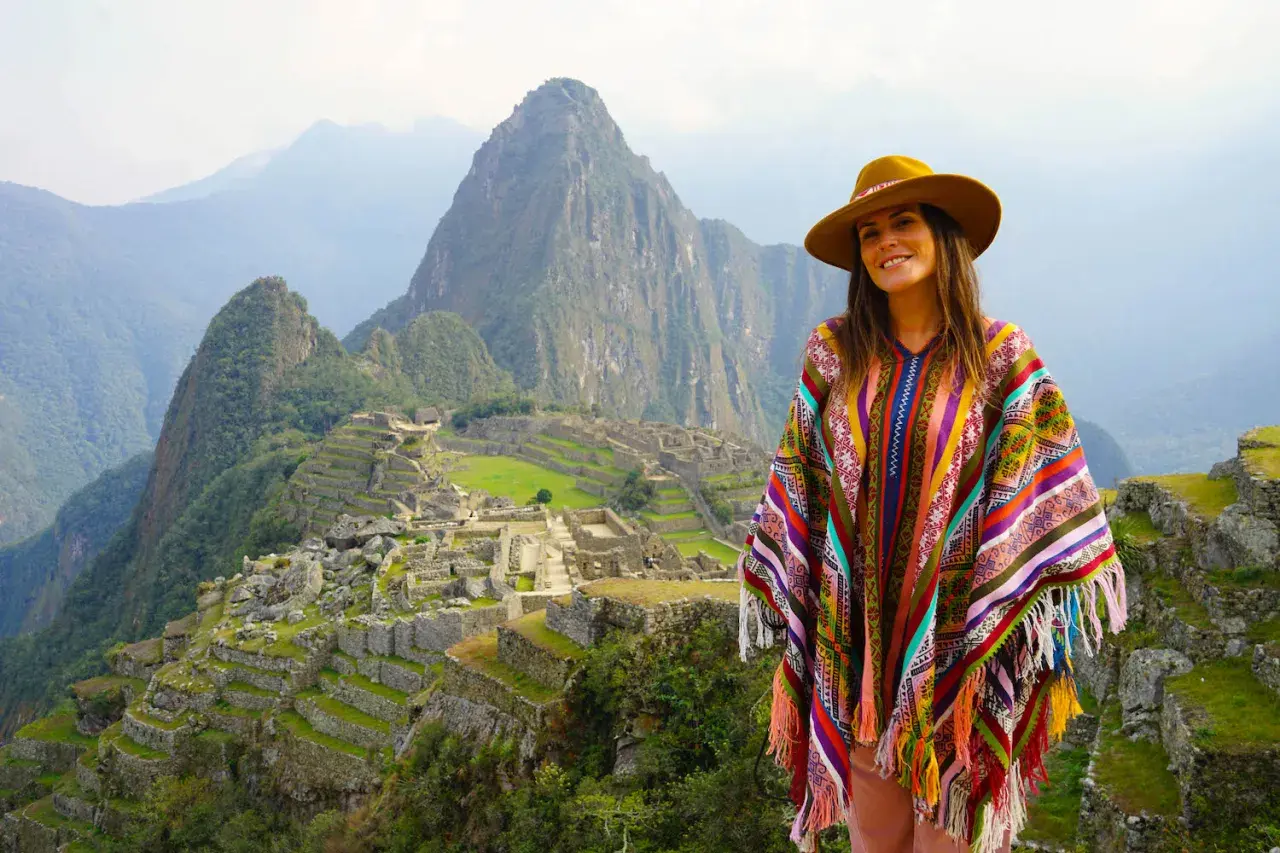 Mujer con poncho colorido y sombrero en Machu Picchu, una experiencia inolvidable al viajar a Perú.