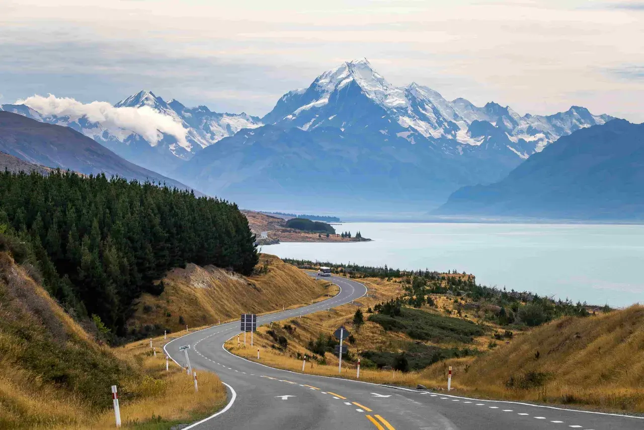 Carretera serpenteante hacia montañas nevadas y un lago turquesa. Impresionantes vistas de Nueva Zelanda que ver.