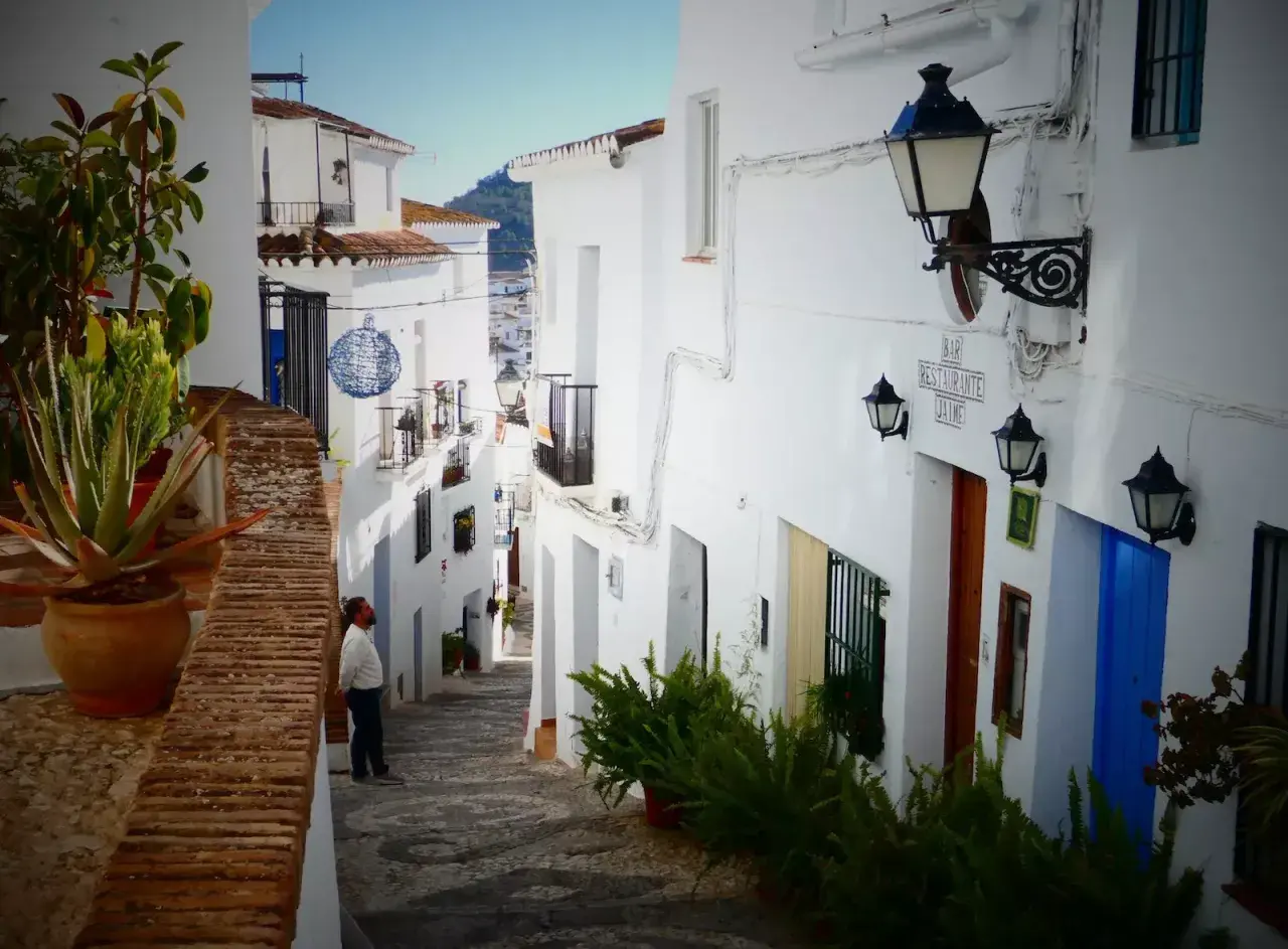 Hombre mira callejuela blanca en Frigiliana. Aquí puedes encontrar dónde comer en Frigiliana, con un bar y restaurante.