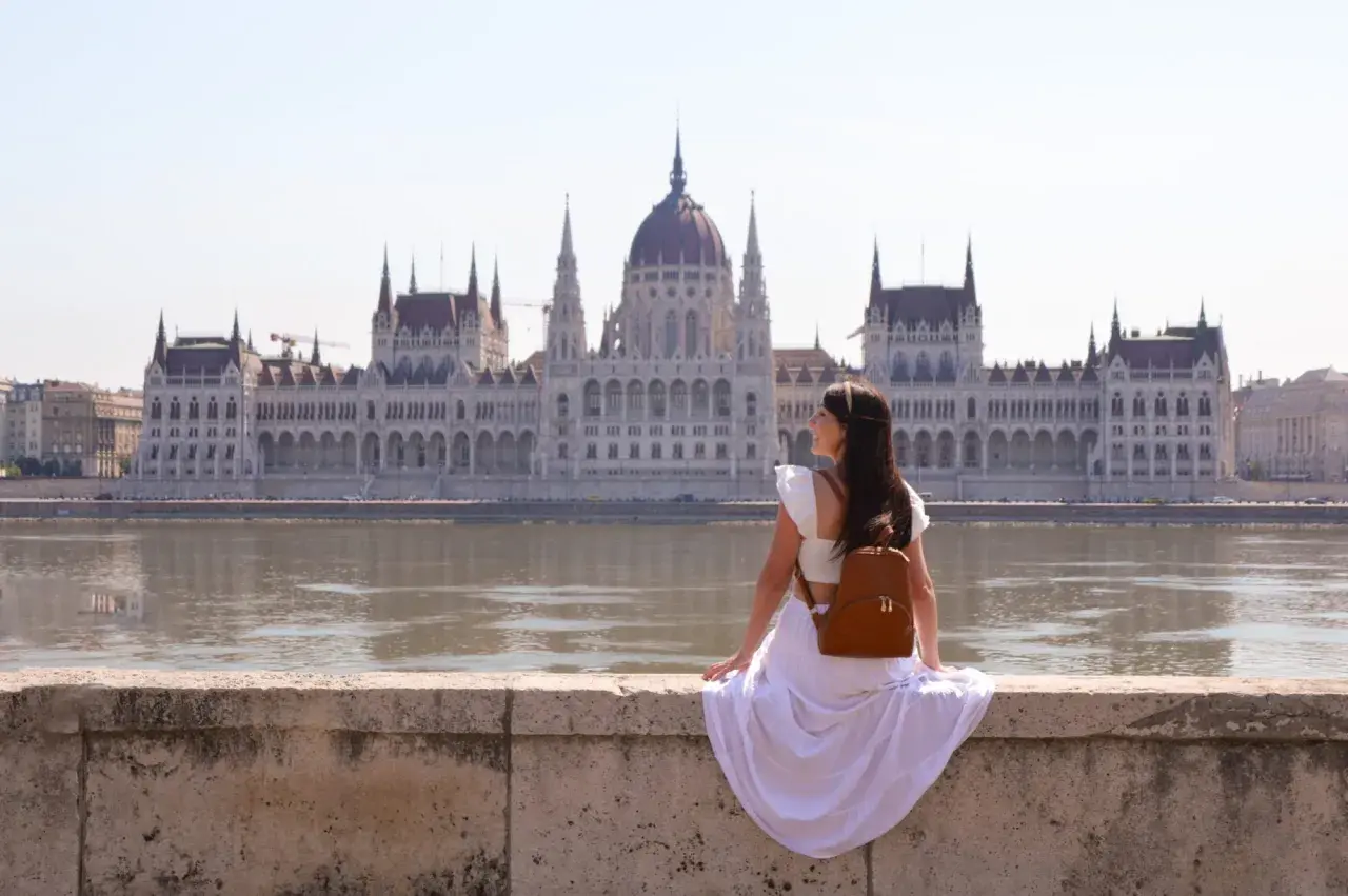 Mujer con mochila admira el Parlamento de Budapest, un lugar imprescindible que ver en Budapest.