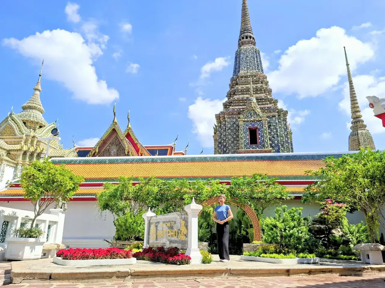 Disfrutando de un free tour en Bangkok, una mujer posa frente a templos tailandeses y pagodas ornamentadas bajo un cielo azul.
