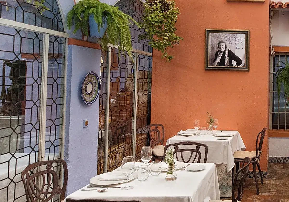 Mesas puestas en un patio andaluz, ideal para saber donde comer en Córdoba. Un retrato adorna la pared naranja.