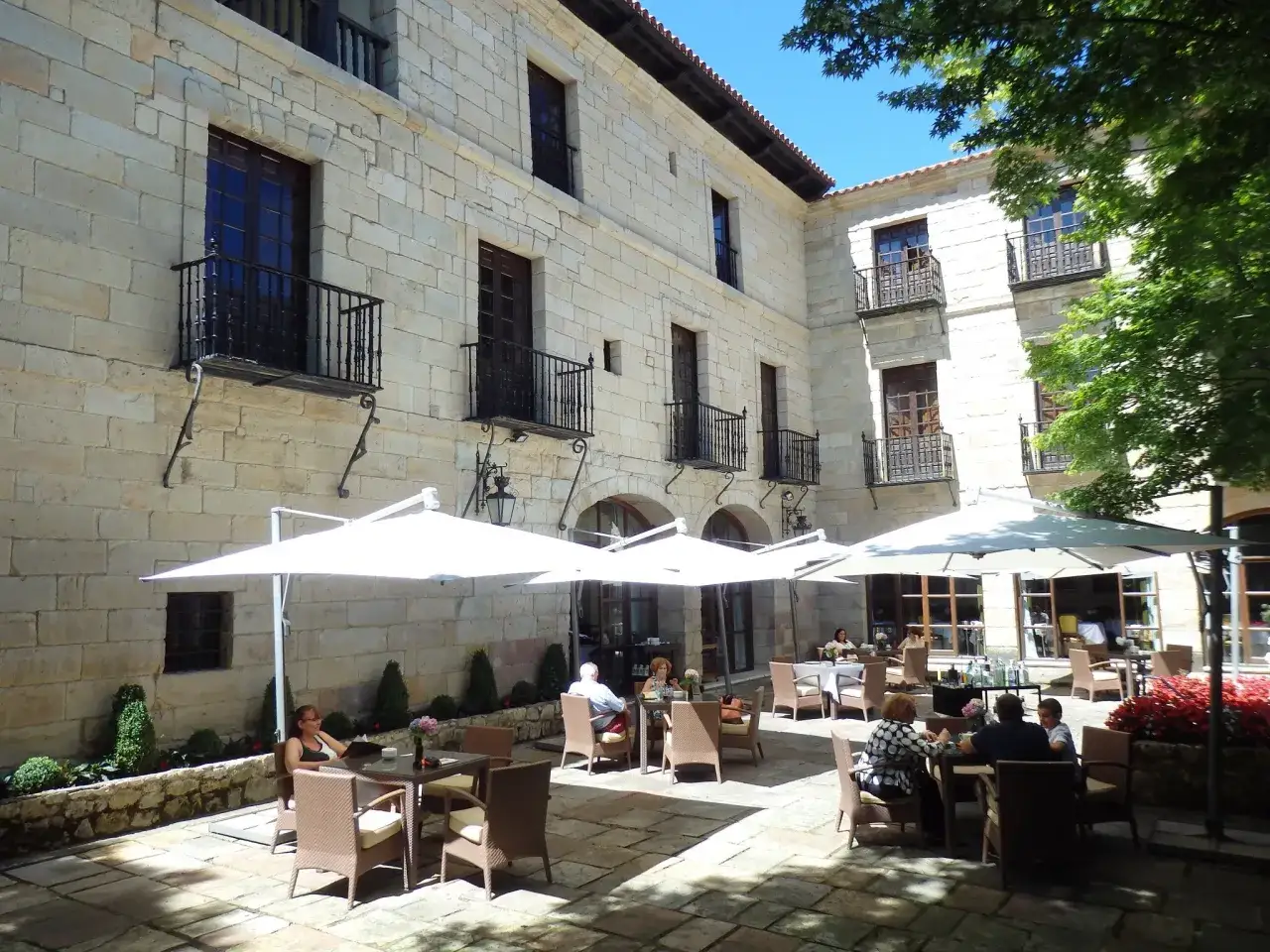 Disfruta de un día soleado donde comer en Santillana del Mar, con mesas al aire libre bajo sombrillas blancas, rodeado de arquitectura de piedra.