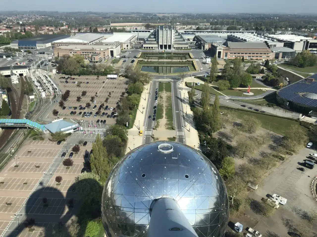 Vista a&eacute;rea del Atomium, un lugar ic&oacute;nico para viajar a Bruselas. Se aprecian edificios, estacionamientos y un estanque.