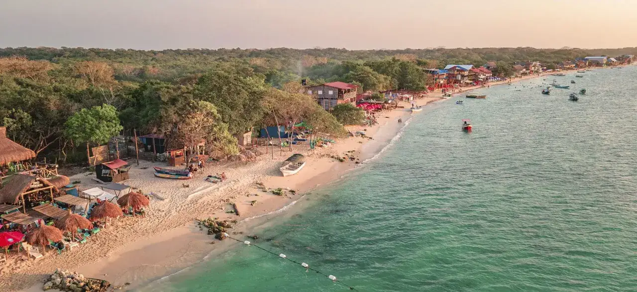 Playa caribe&ntilde;a con palapas, gente disfrutando y botes en el mar turquesa. &iexcl;La mejor &eacute;poca para viajar a Colombia es ahora!