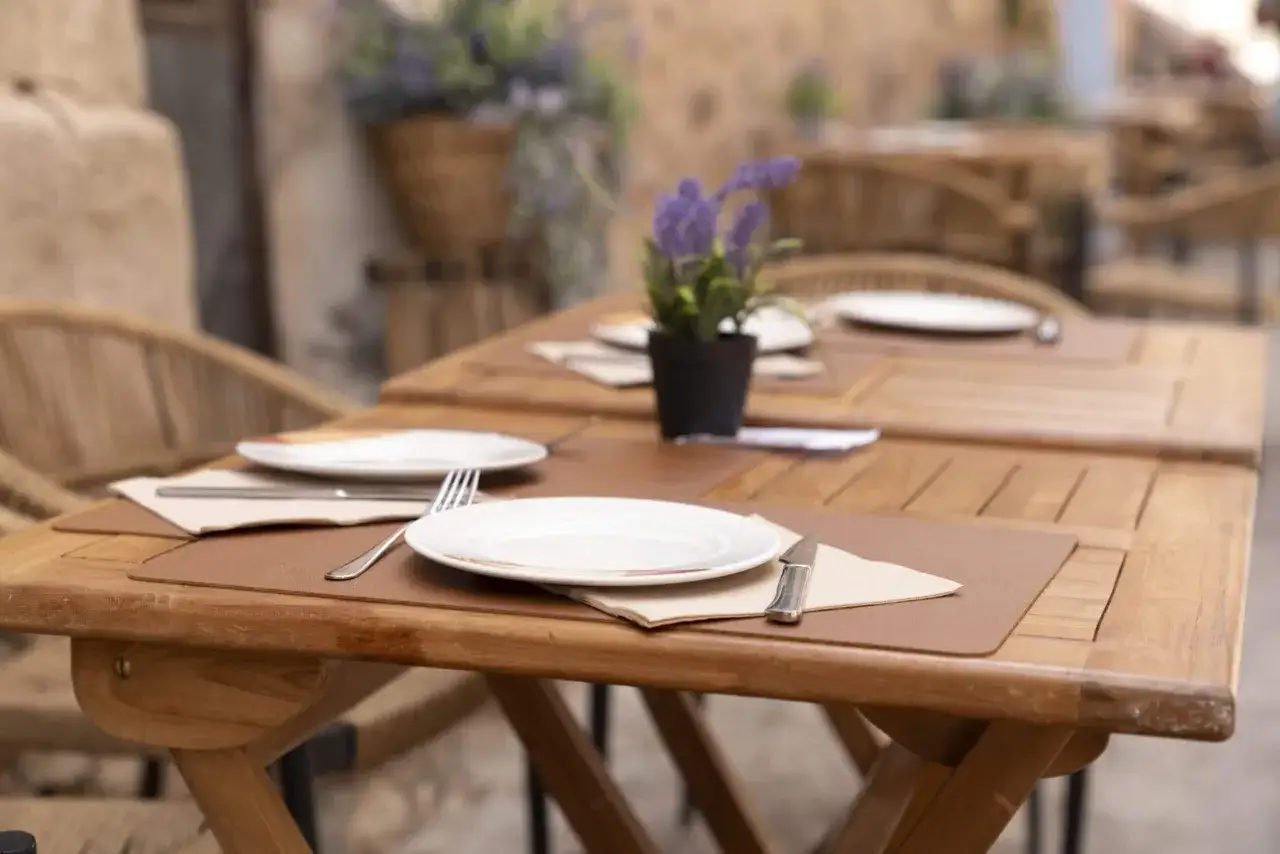 Mesas de madera al aire libre, listas para disfrutar de dónde comer en Albarracín. Flores moradas decoran el ambiente.
