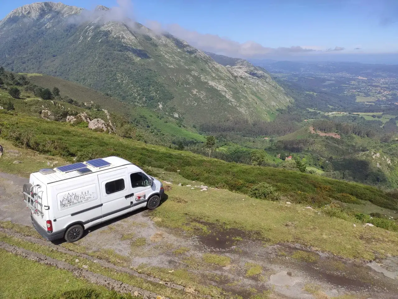 Furgoneta camperizada con paneles solares aparcada en un paisaje monta&ntilde;oso, lista para viajar.