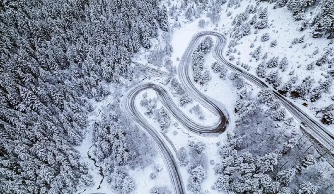Carretera sinuosa cubierta de nieve, ideal para viajar a Andorra. Bosques nevados y un camino que serpentea entre ellos.