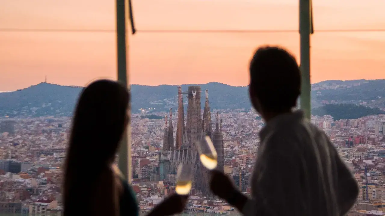 Pareja brinda con copas de champán en el mirador de la Torre Glòries, contemplando la Sagrada Familia al atardecer.