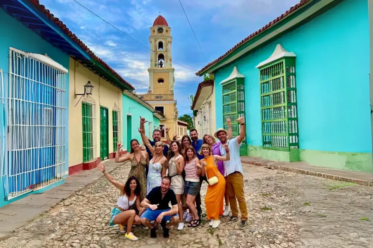 Grupo de amigos sonríe y saluda en una calle empedrada de Trinidad, Cuba. ¡Es seguro viajar a Cuba y disfrutar de su colorida arquitectura!