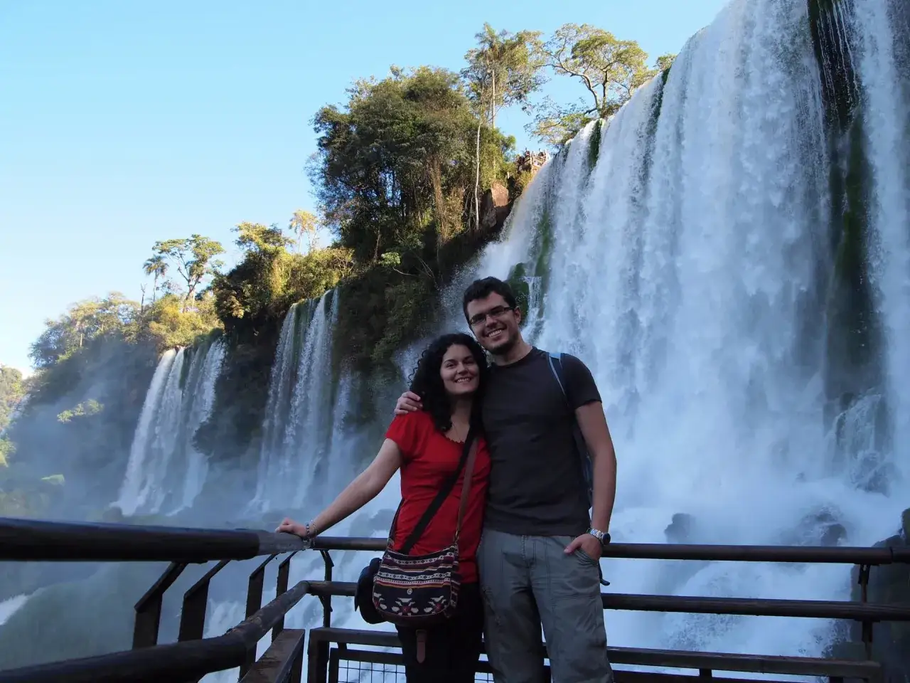 Pareja sonriente frente a las Cataratas del Iguazú, un imperdible que ver en Argentina.