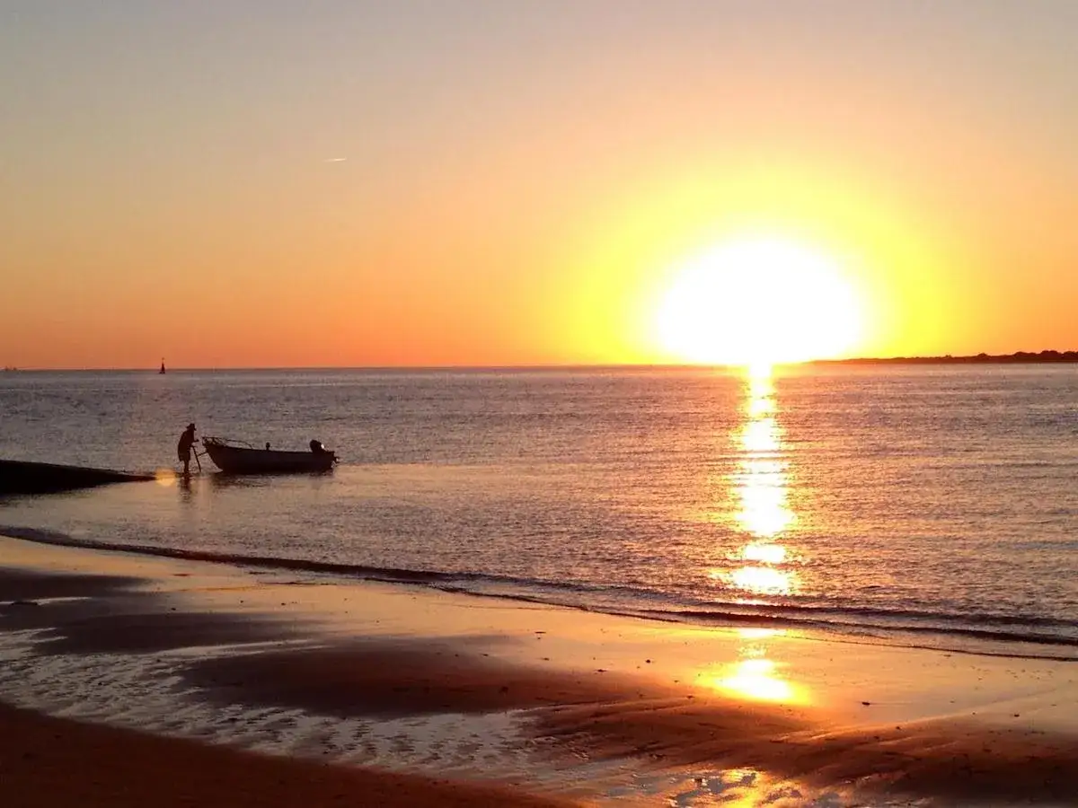 Atardecer en Sanl&uacute;car de Barrameda. Un pescador empuja su barca en la orilla mientras el sol se pone. Imprescindible que ver en Sanl&uacute;car de Barrameda.