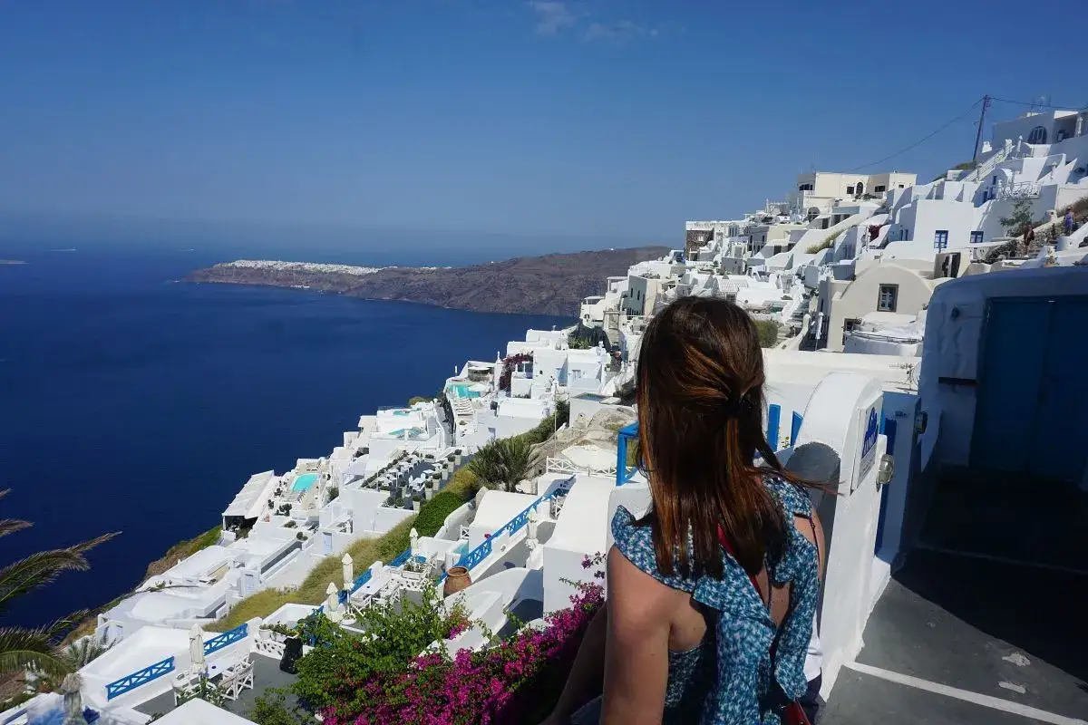 Mujer admira la vista de casas blancas en Santorini, un lugar imprescindible que ver en Santorini.
