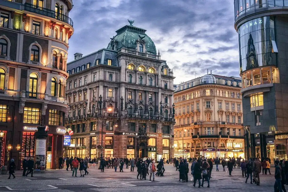 Gente paseando por una plaza de Viena al anochecer, con edificios históricos y modernos. Ideal para un free tour Viena.