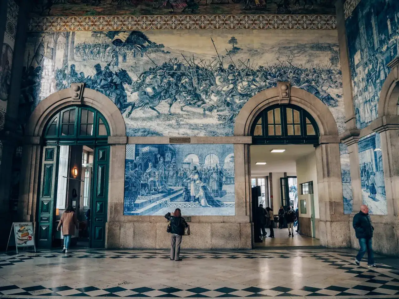 Un free tour Oporto te lleva a admirar azulejos históricos. Gente observa murales de batallas y escenas cortesanas.