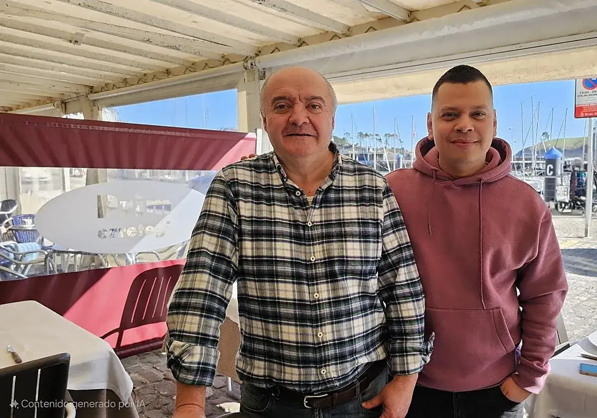 Dos hombres sonríen en un restaurante con vistas al puerto de Lekeitio, listos para comer.