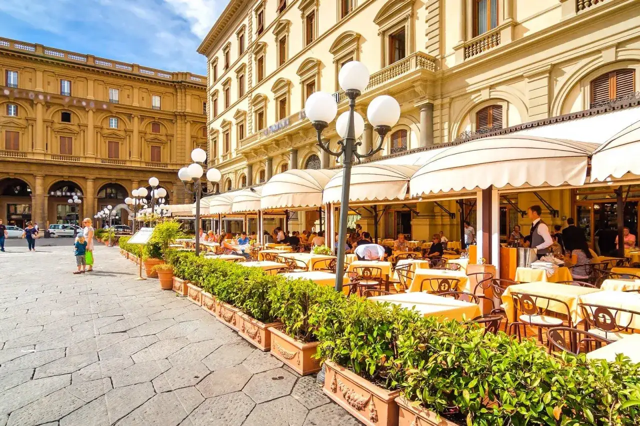 Un café al aire libre en Florencia, perfecto para decidir dónde comer en Florencia. Mesas amarillas bajo toldos, gente disfrutando.