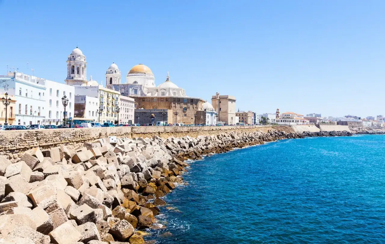 Costa de Cádiz con la Catedral al fondo. Ideas de qué ver en Cádiz en un día: paseo marítimo, edificios blancos y mar azul.