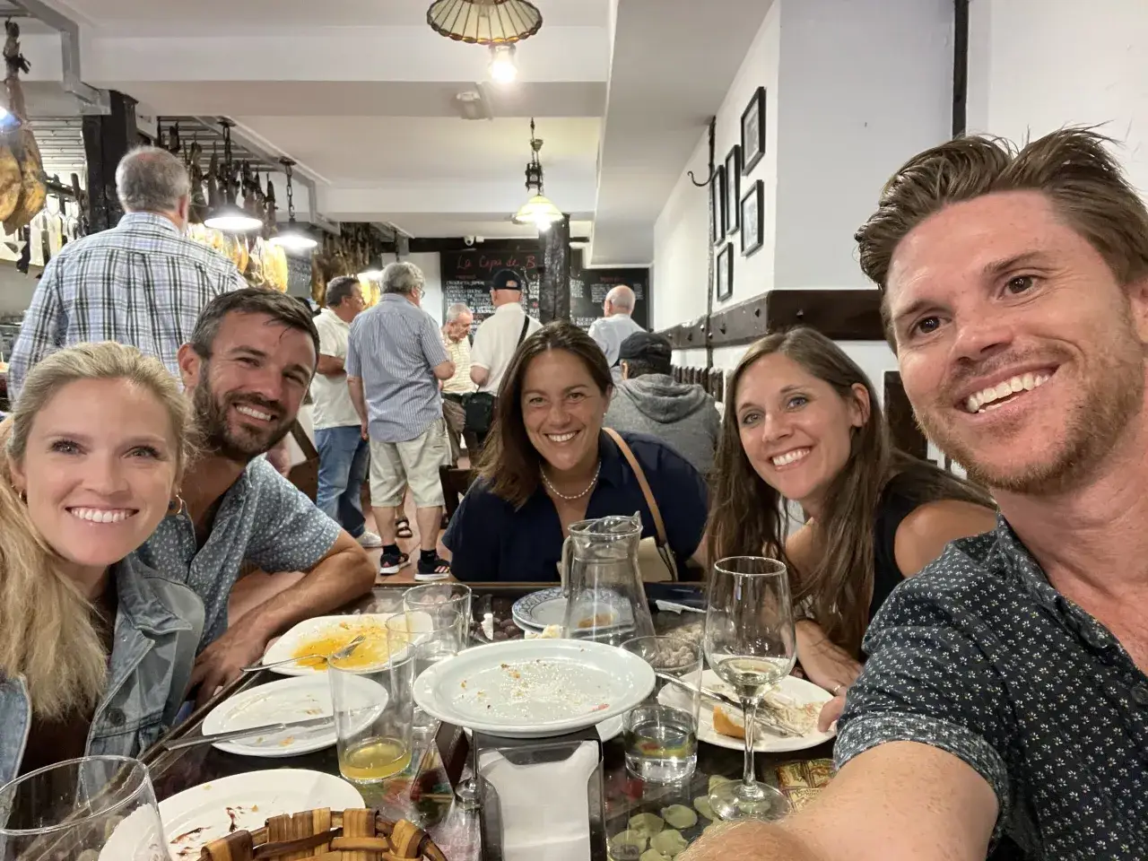 Amigos disfrutando de una comida después de un free tour en San Sebastián. El restaurante tiene jamones colgados y un ambiente animado.