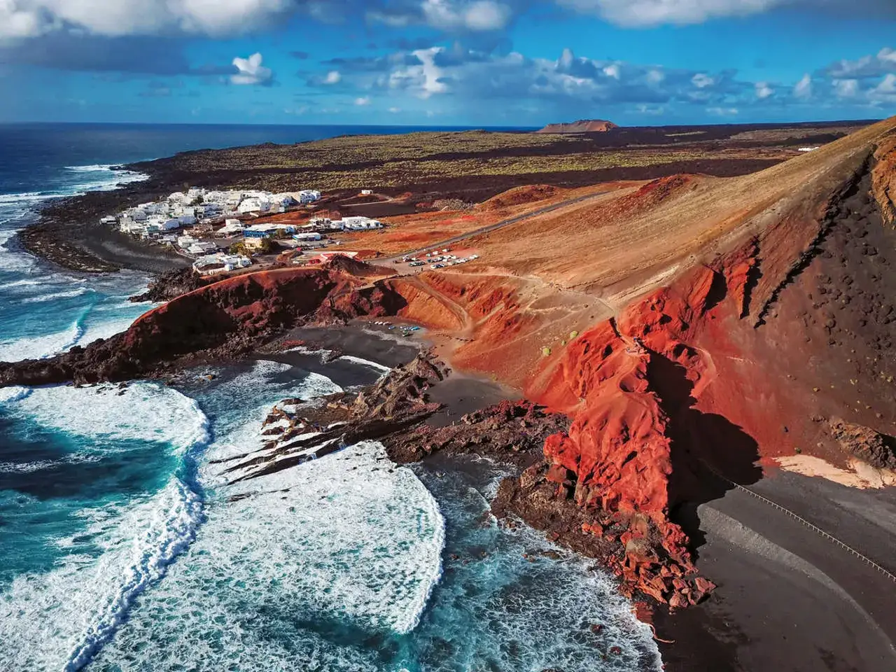 Paisaje volc&aacute;nico en Lanzarote con un pueblo blanco junto al mar azul. &iexcl;Ideal para viajar a Lanzarote!