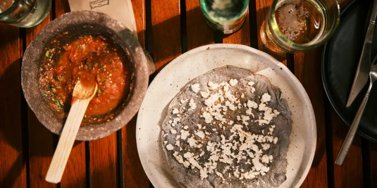Un tlayoyo de maíz azul con queso fresco y salsa roja en molcajete. Una probadita de lo que puedes ver en México.