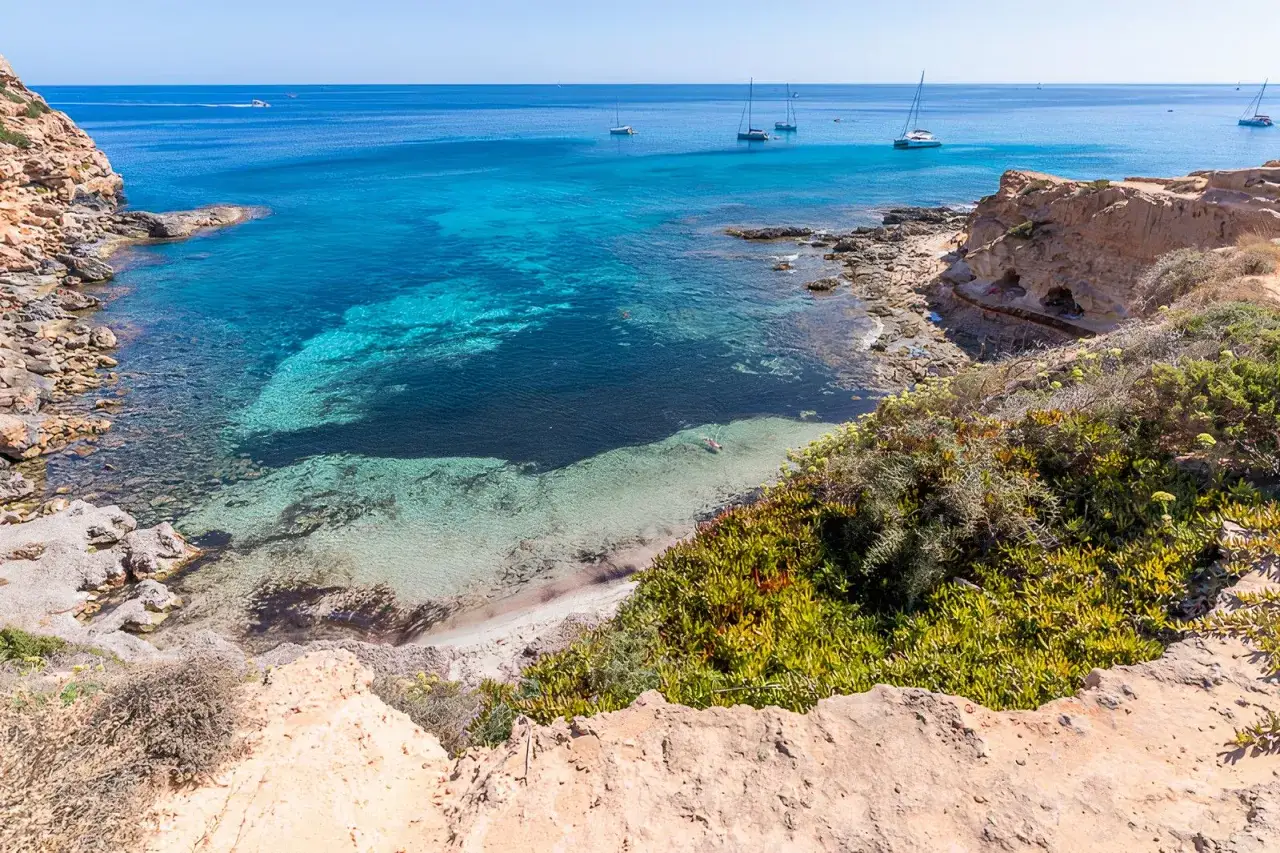 Calas de aguas turquesas y arena dorada, veleros navegando. Un d&iacute;a perfecto para descubrir qu&eacute; ver en Formentera.