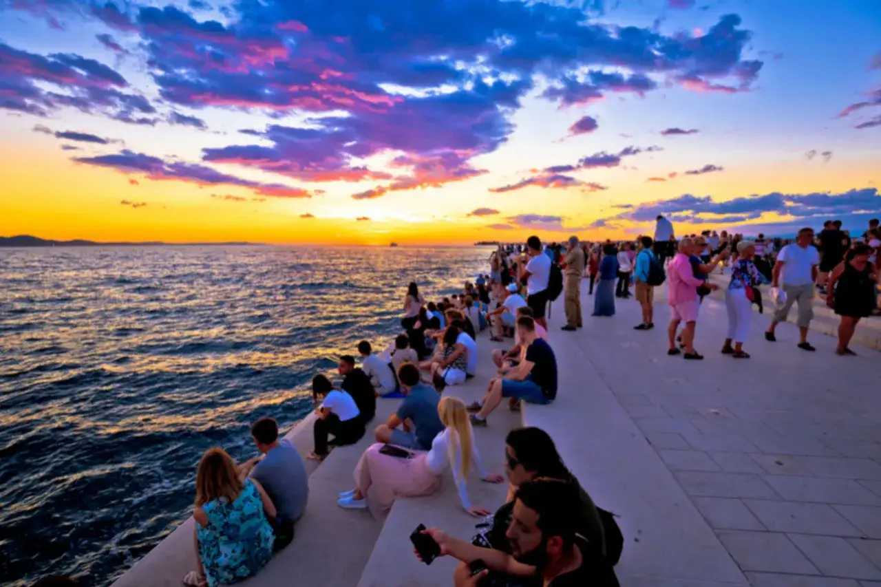 Gente sentada en el paseo marítimo de Zadar, disfrutando de una espectacular puesta de sol sobre el mar Adriático. Un momento perfecto para ver en Zadar.