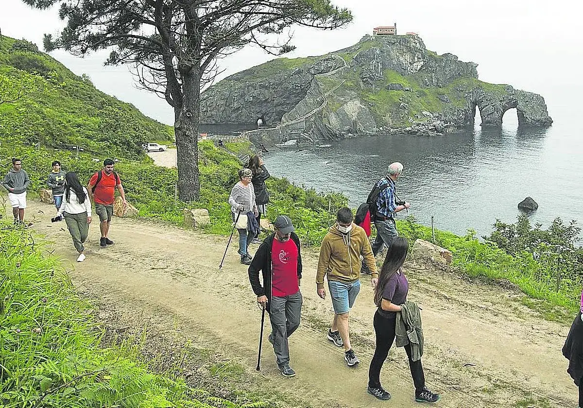 Senderos verdes y rocosos que llevan a San Juan de Gaztelugatxe, un lugar imprescindible que ver en Bermeo. Turistas disfrutan del paisaje.