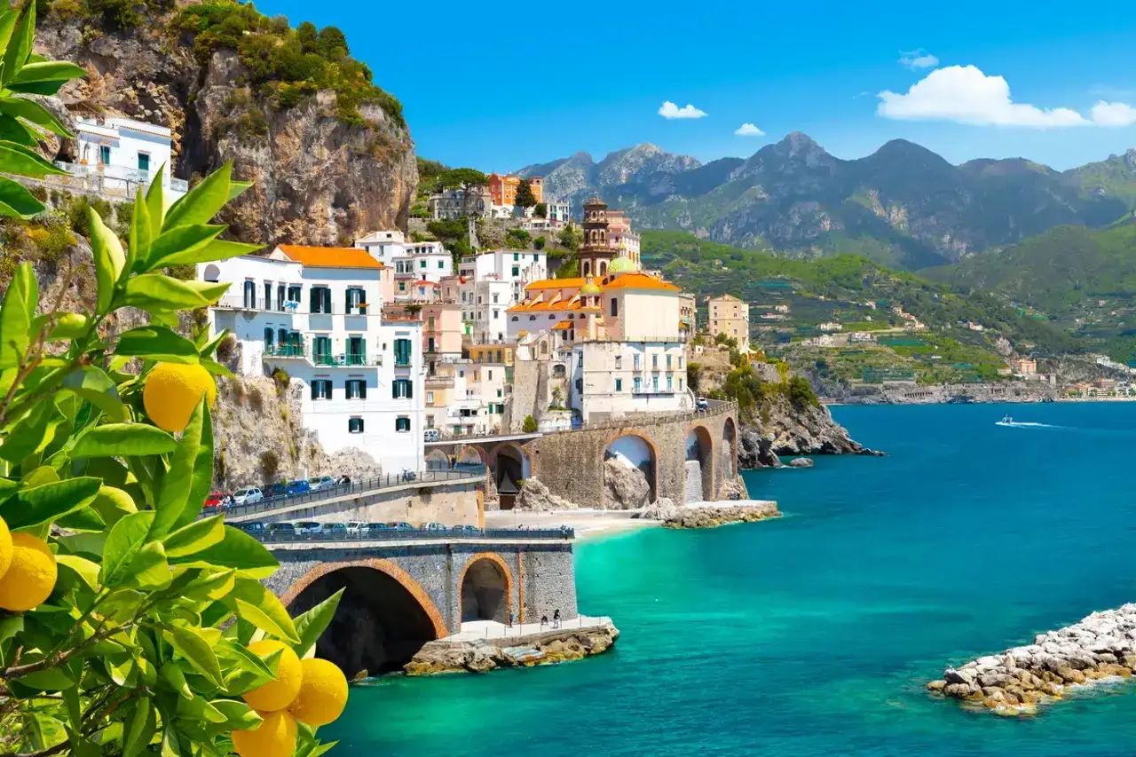 Pueblos de la costa Amalfitana, con casas blancas y coloridas aferradas a acantilados, mar turquesa y limoneros en primer plano.