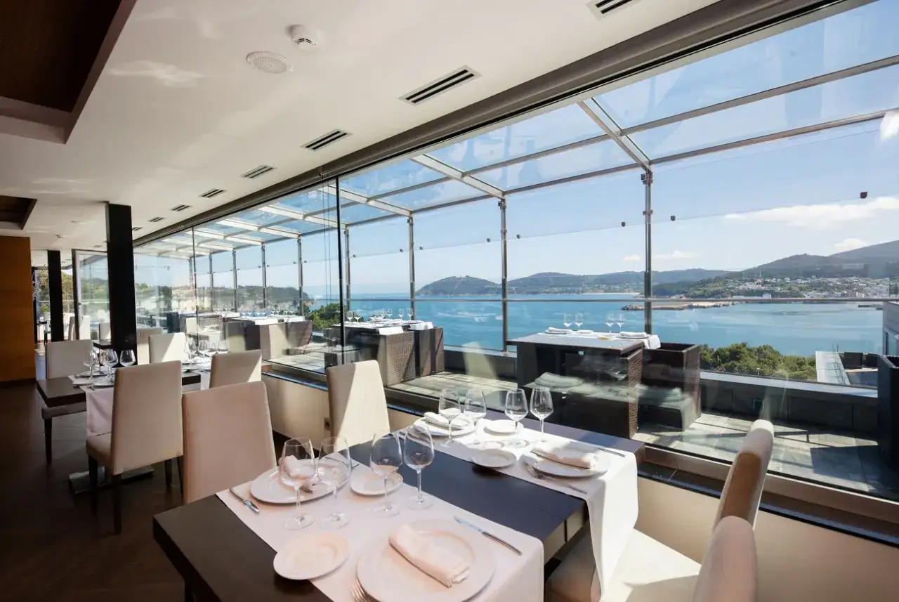 Elegante comedor con vistas al mar, ideal para saber donde comer en Viveiro. Mesas puestas y ambiente acogedor.