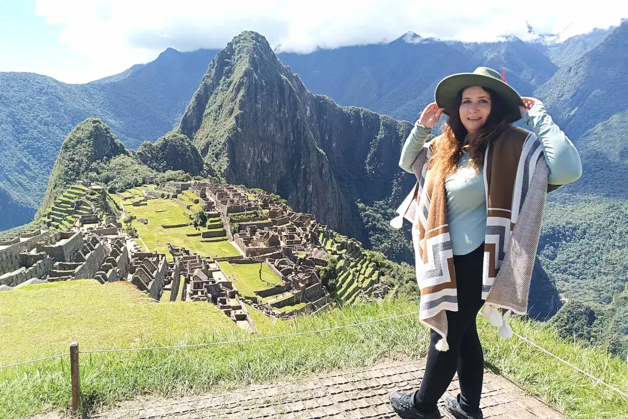 Mujer con sombrero y poncho disfruta de la vista de Machu Picchu, una experiencia inolvidable al viajar a Perú.