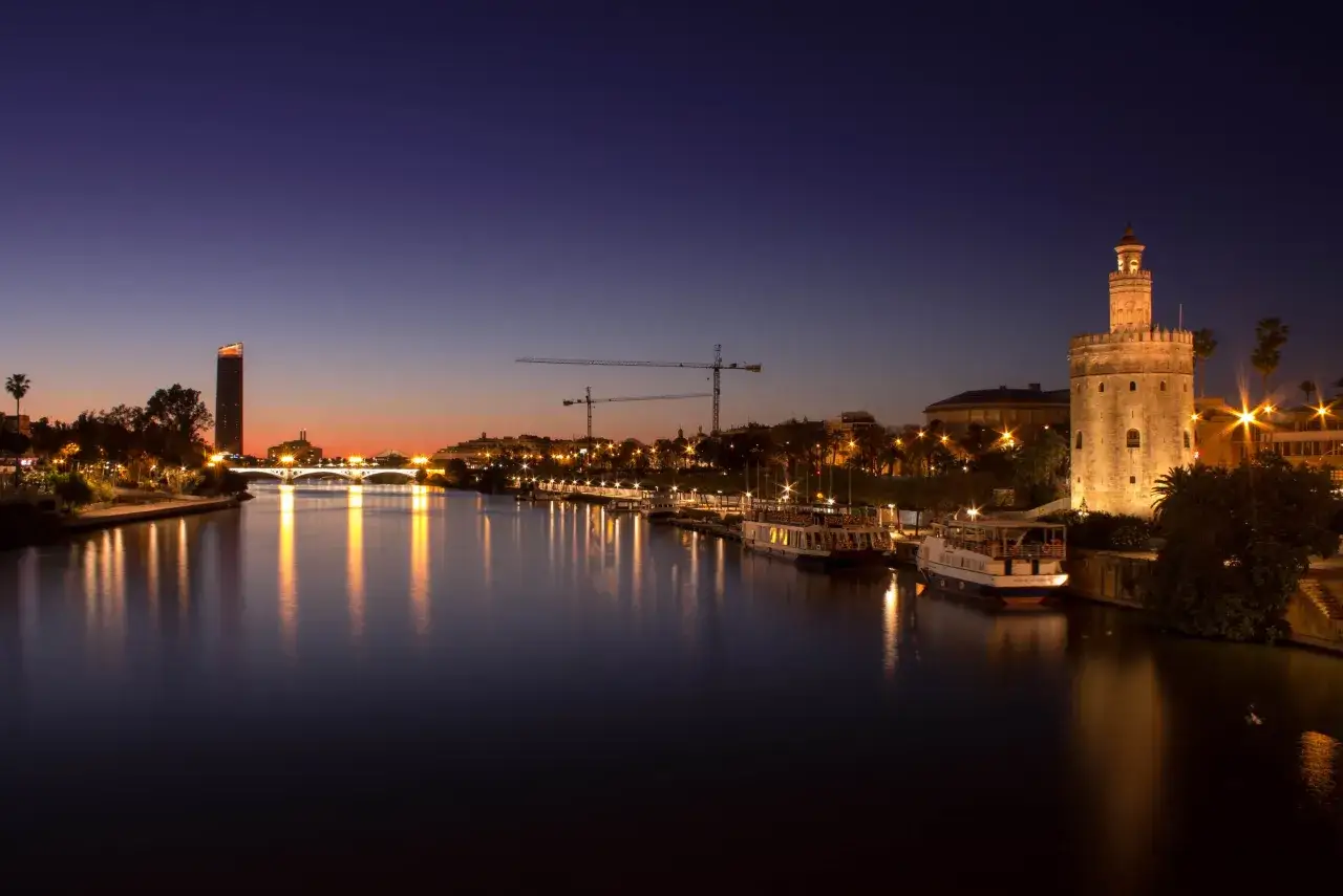 Atardecer en Sevilla, con la Torre del Oro iluminada y reflejos en el río. Un plan perfecto para ver Sevilla en 2 días.